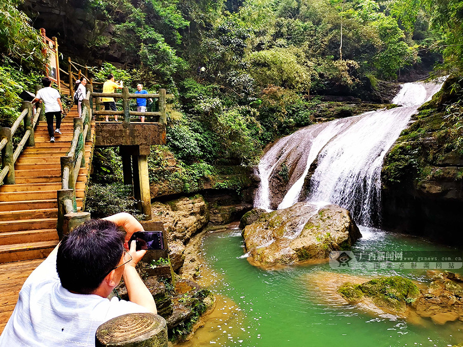 遊客在環江毛南族自治縣牛角寨景區的「三疊泉」瀑布遊玩拍照。